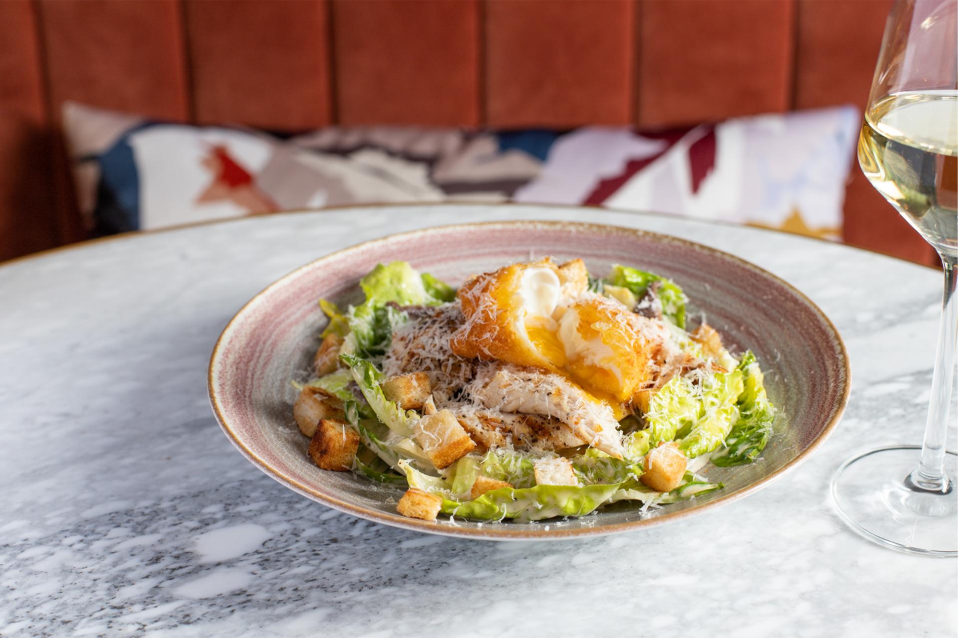 A bowl of salad with a glass of wine next to it.