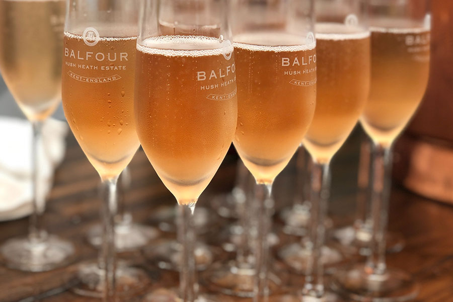 Several flutes of sparkling wine set on a table, each glass marked with "Balfour" and "Hush Heath Estate.