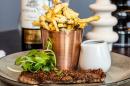 A steak with fries and a bottle of wine on a plate.