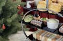 A tiered tray with sandwiches and pastries in front of a christmas tree.