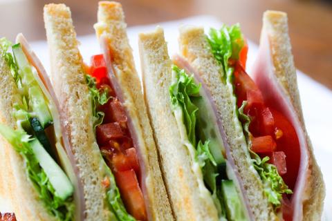 Close-up of three club sandwiches filled with ham, lettuce, tomato, cucumber, and a spread between white bread slices.