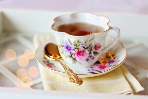 A floral-patterned teacup filled with tea, placed on a matching saucer with a gold spoon, rests on a folded yellow napkin.